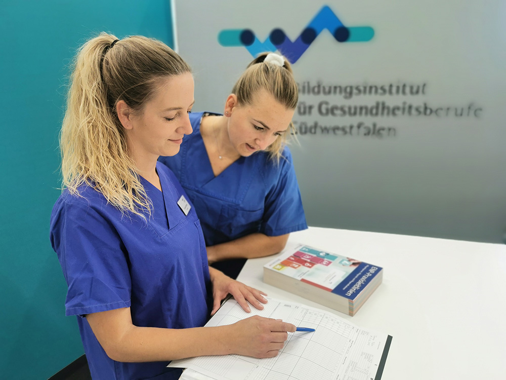Zwei Auszubildende in blauen Kitteln sprechen im Aufenthaltsraum des BiGS über Ausbildungsinhalte