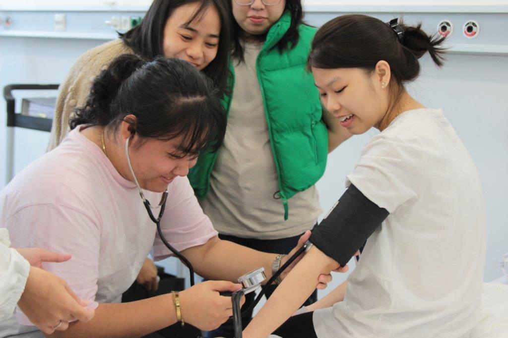 Vier vietnamesische Auszubildende üben im SkillsLab mit einem Blutdruckmessgerät
