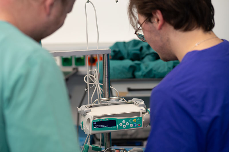Zwei Auszubildende in grünem und blauem Kittel bedienen einen medizinischen Apparat im SkillsLab