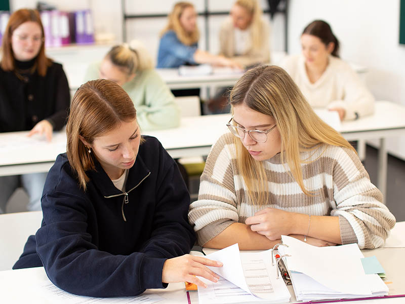 Zwei Auszubildende in Freizeitkleidung bearbeiten im Klassenraum ihren Ausbildungsnachweis